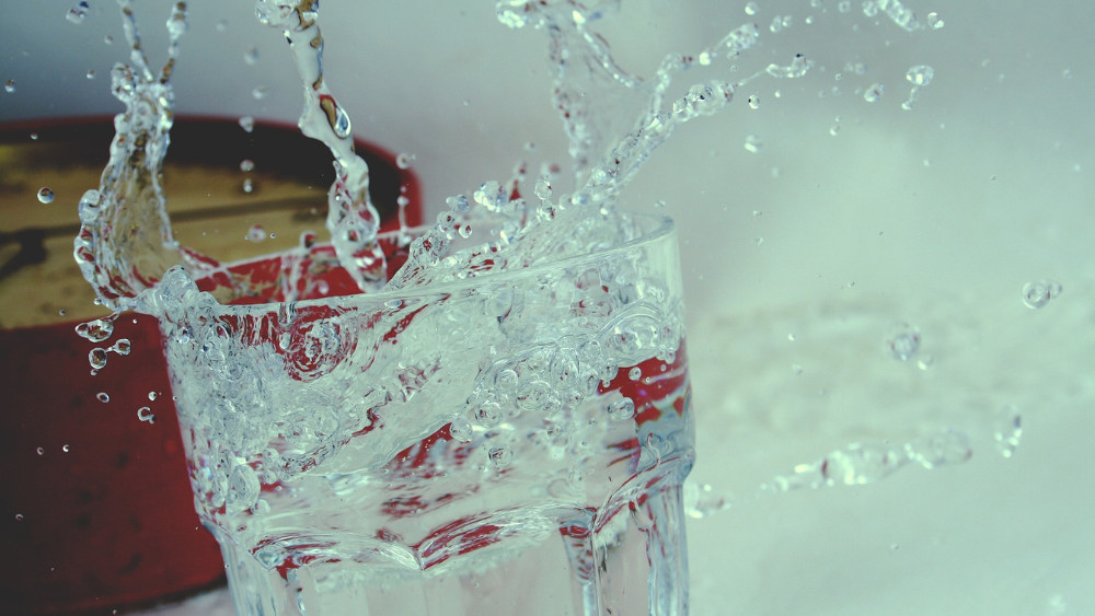 Glas Wasser mit Uhr im Hintergrund (Symbolbild): Leitungswasser haltbar machen